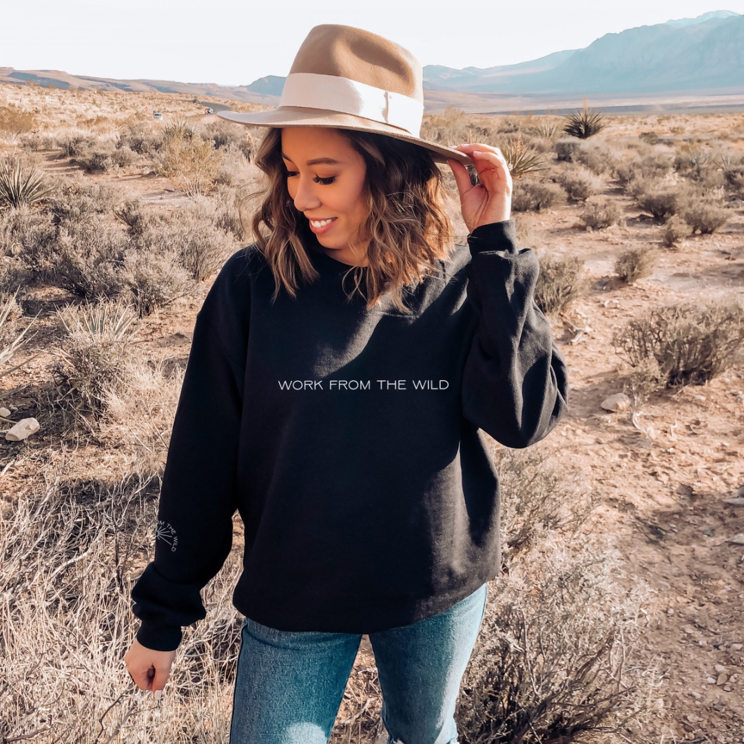 Woman in a large hat and black sweatshirt standing out in a desert.