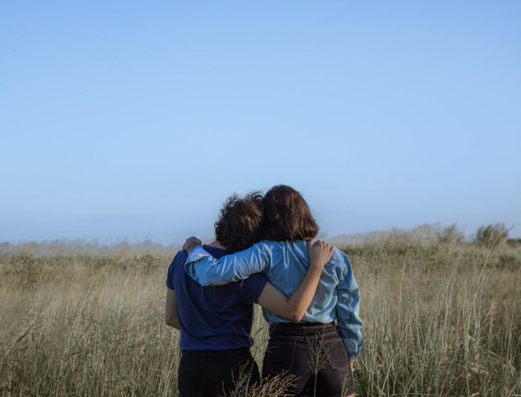 Two people standing in a field with their arms around each other's shoulders. 