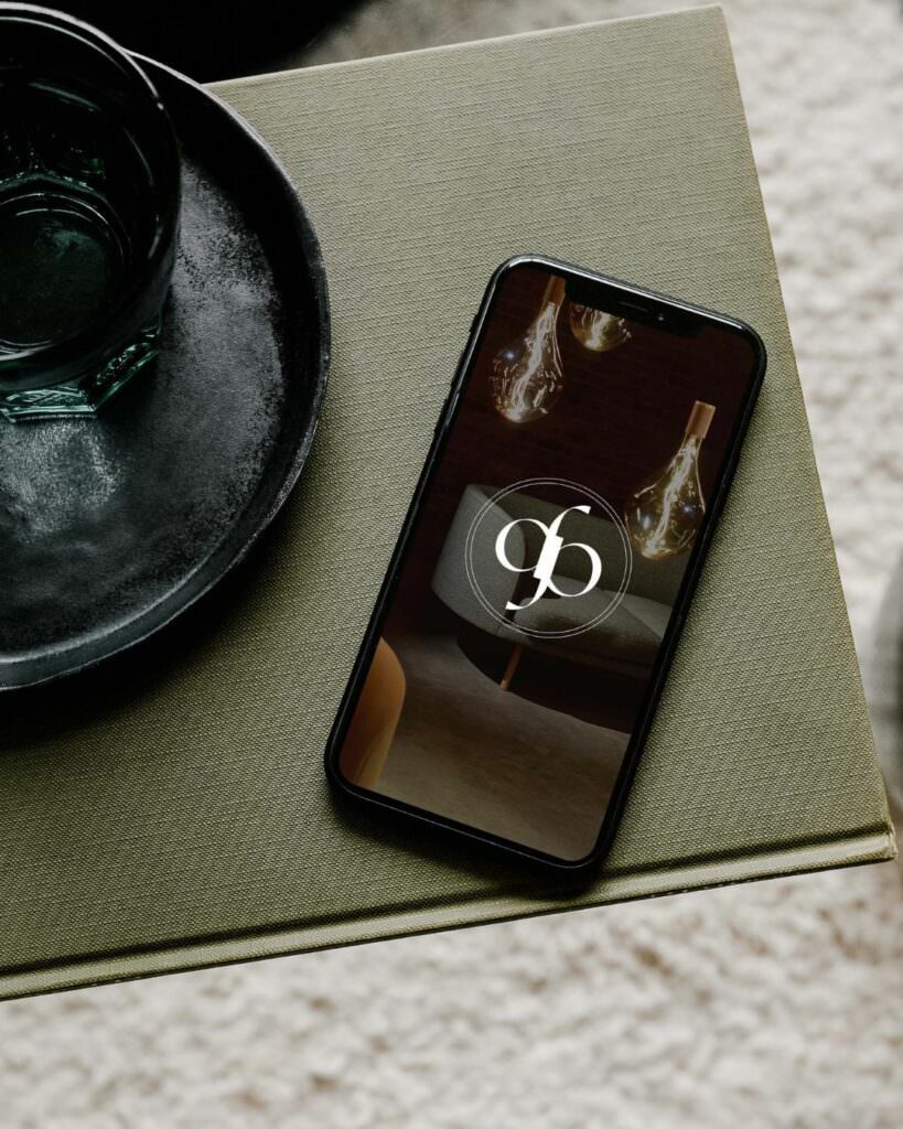 A phone laying on a book next to a glass of water with a brand logo pulled up on the screen.