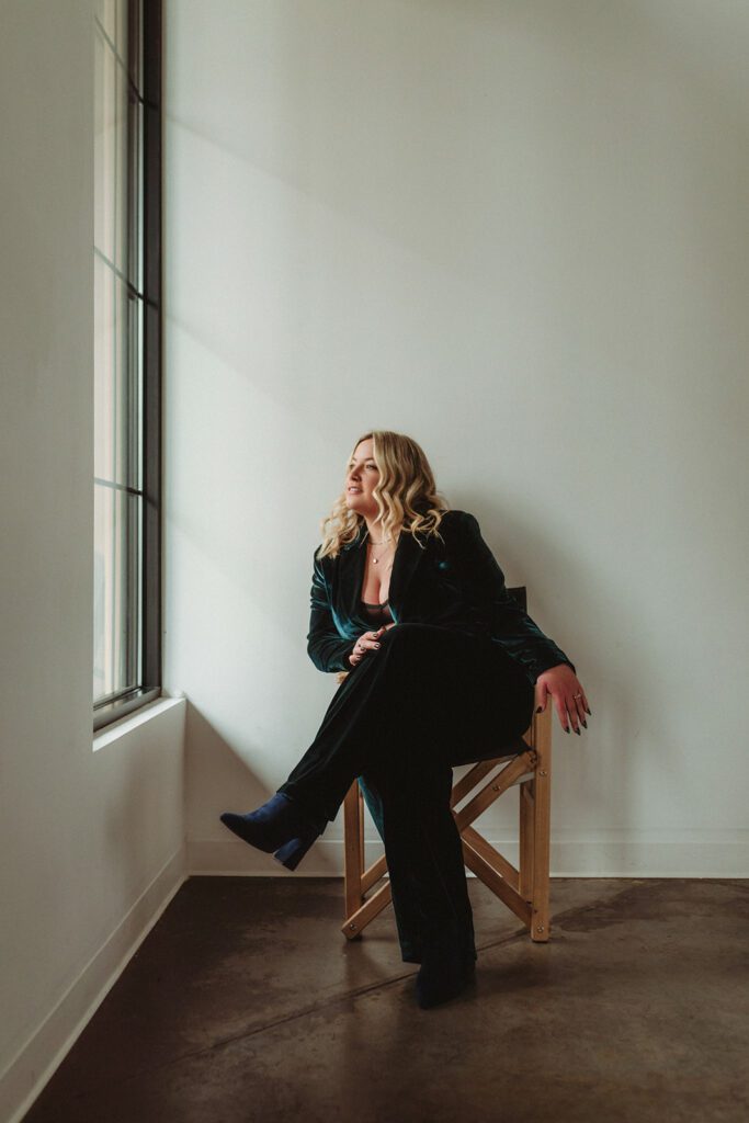 Bethany McCamish, creator of the brand strategy masterclass, in a suit sitting in a chair and looking out a window.