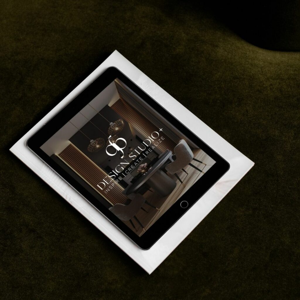 An iPad sitting on a white book on a couch. On the iPad is an image of a luxury dining room with a logo on top that reads "dp Design Studio+. Inspire | Create | Realize".