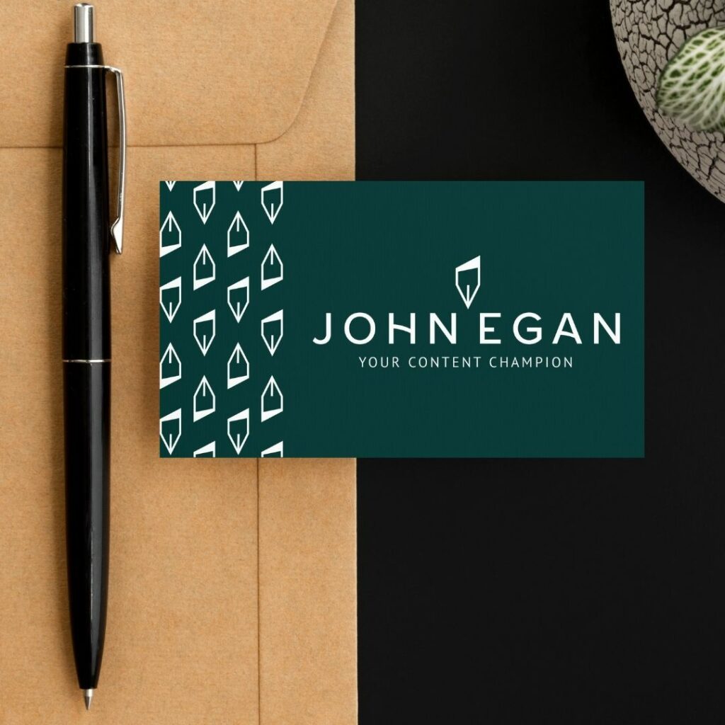A pen sitting next to a business card. On the card is the logo for "John Egan. Your content champion".