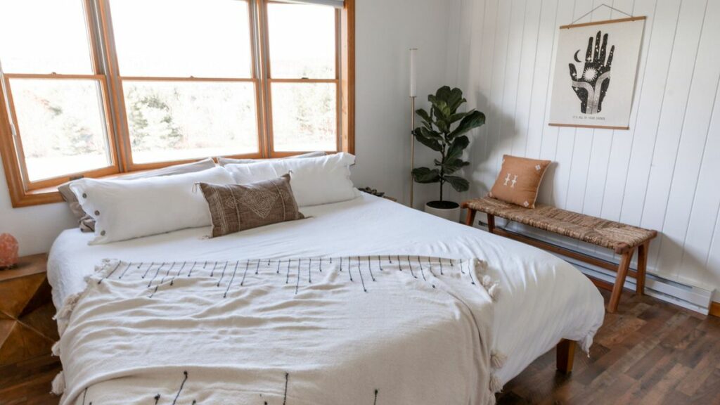bed with white blankets on it in a room with windows covering one wall 