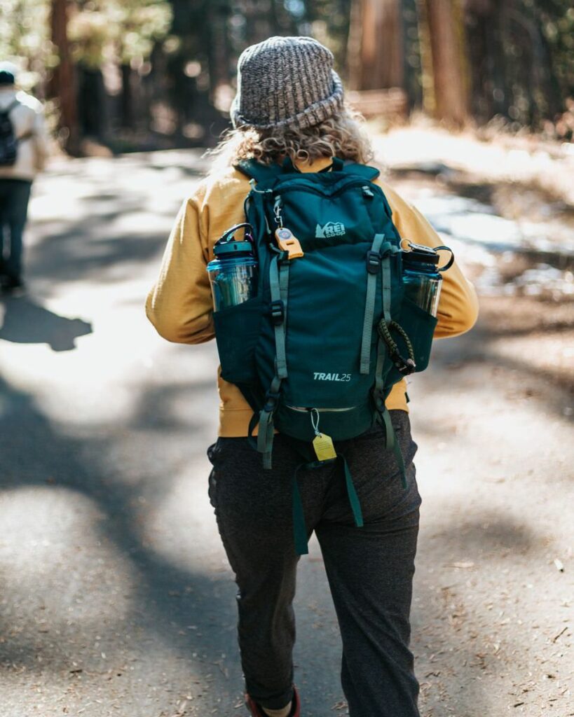 Woman with a teal backpack hiking along a trail in the woods 

