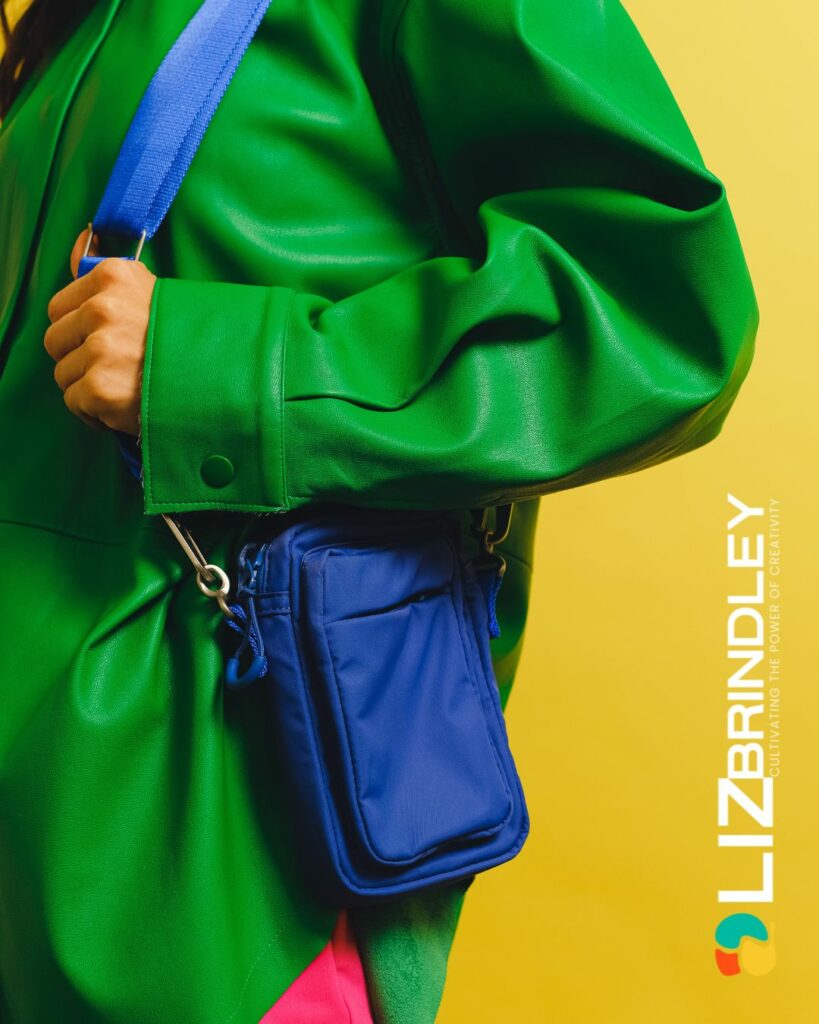 A close-up of a bright green jacket with a blue pouch over a multicolored outfit, featuring the branding 'Liz Brindley' with a focus on vibrant, creative expression.