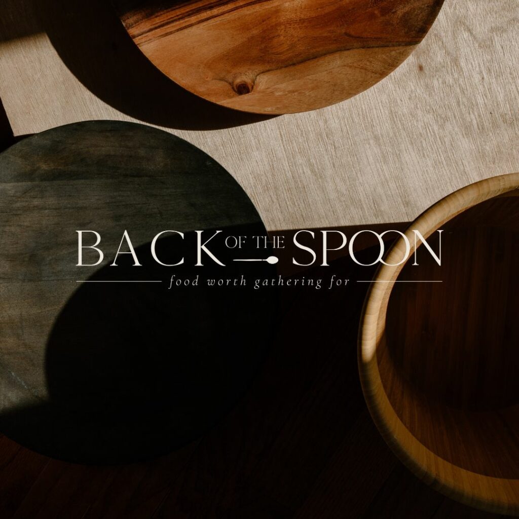 Dark image of wooden bowls with a logo on top that reads "Back of the Spoon. Food worth gathering for".