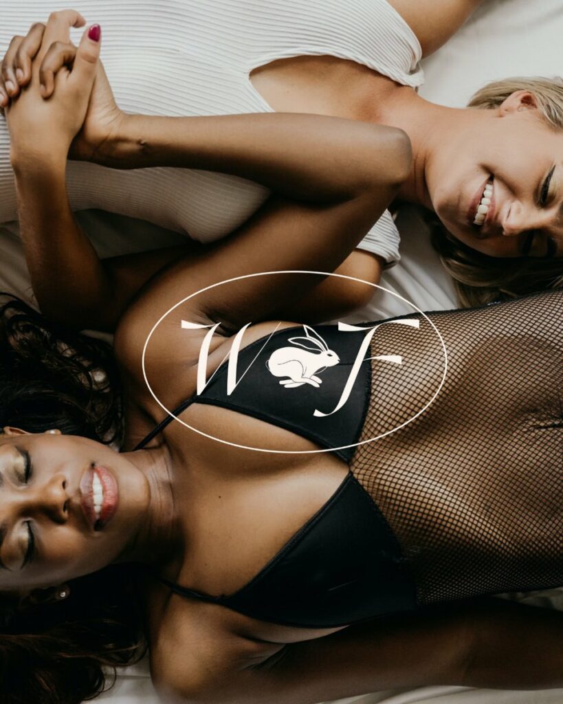 Two women laying in opposite directions holding hands with a brand mark on top that has a WF with a hare icon between the letters. 