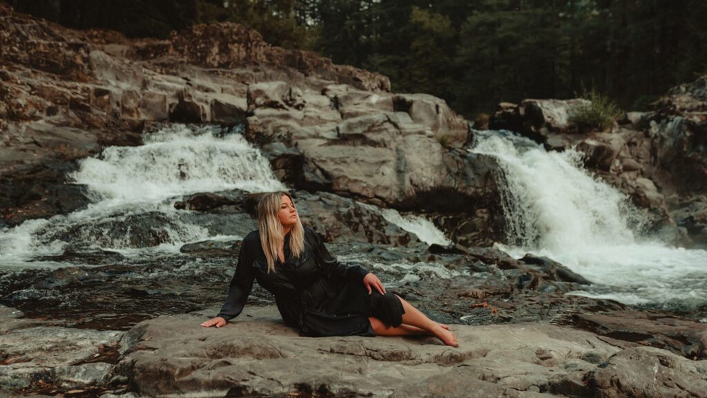 Woman sitting down on rocks with a river running behind her. 
