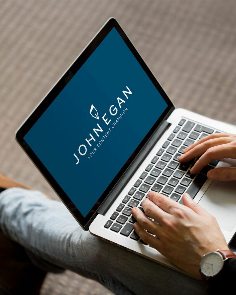 A person typing on their laptop with a logo for John Egan on it. 