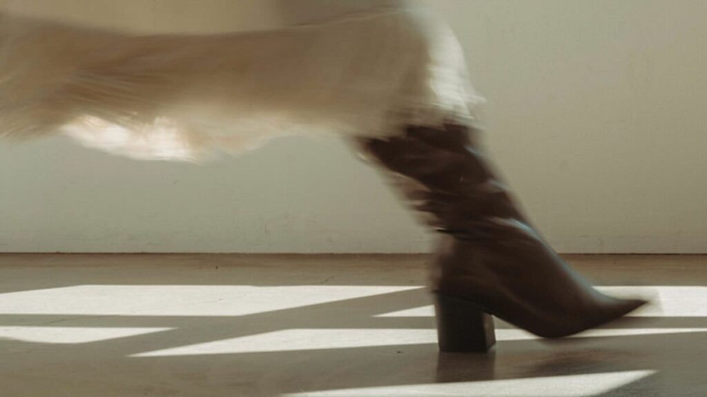 A slightly blurred close up view of a person walking in a brown boot and full length skirt. 