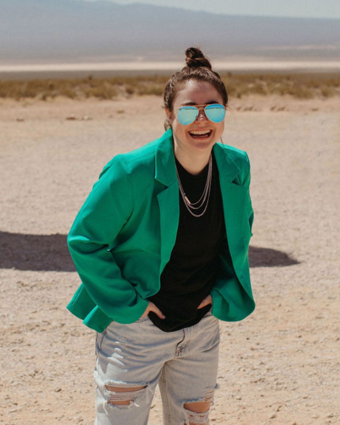 Woman in a green blazer smiling with sunglasses in the desert.