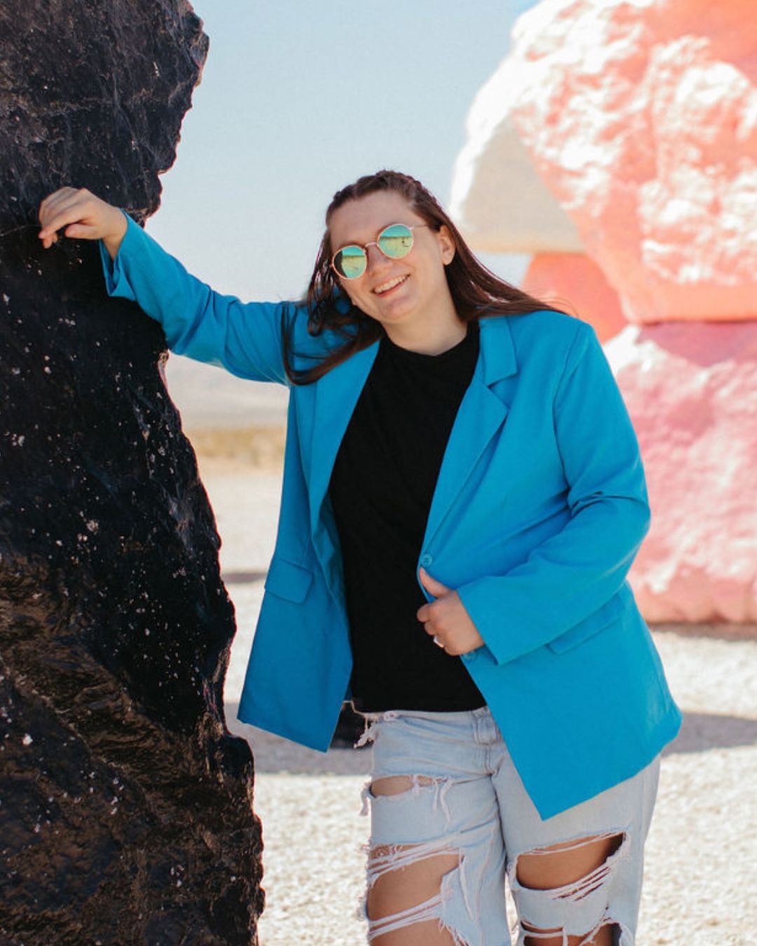 Woman in a blue blazer smiling by colorful rocks.