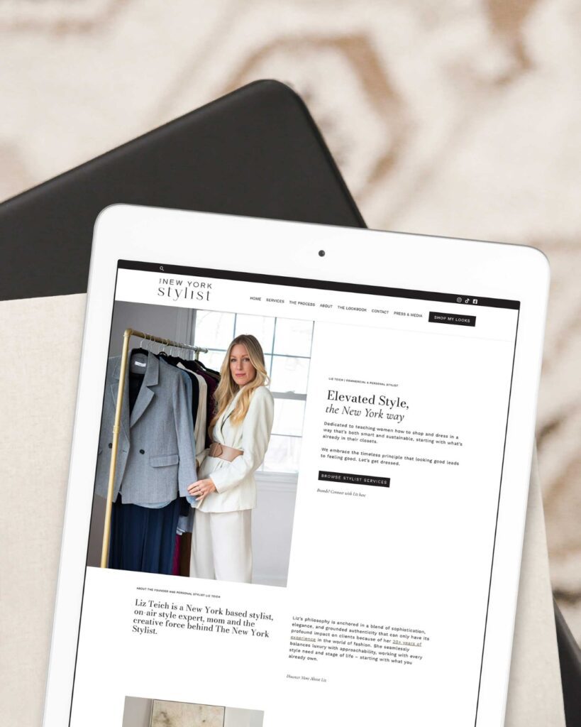 An iPad displaying the homepage of The New York Stylist website, laid on a bed with a minimalist design.