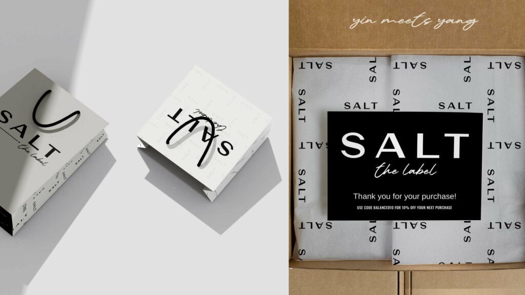 Branding materials for SALT the label are arranged artistically with a minimalist design, including a thank you card, black and white product boxes with bold typography, and a brown shipping box, all embodying the brand's chic and simple aesthetic