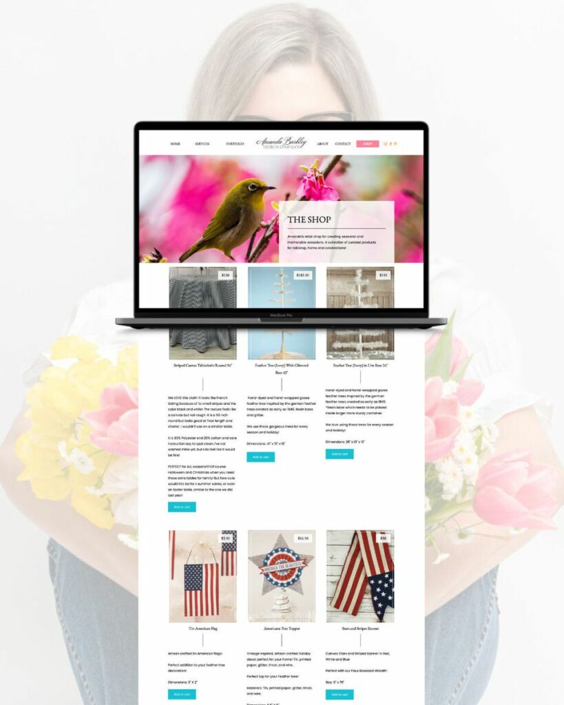 A laptop presenting the front page of a website called 'Amanda Barkley' with a colorful bird and flower banner, while a section below showcases products like flags and decorative items.