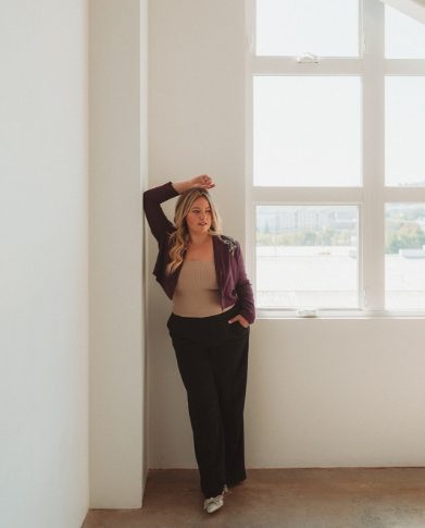 Brand strategist Bethany McCamish leaning against a wall near a window in a maroon blazer.