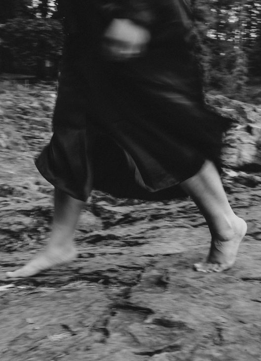 Close up view of someone running barefoot across rocks in a forest.